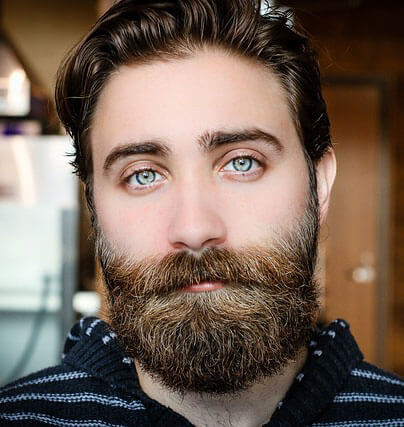 homme avec une barbe et une moustache pleines et épaisses. Il a des yeux bleus saisissants et des cheveux foncés