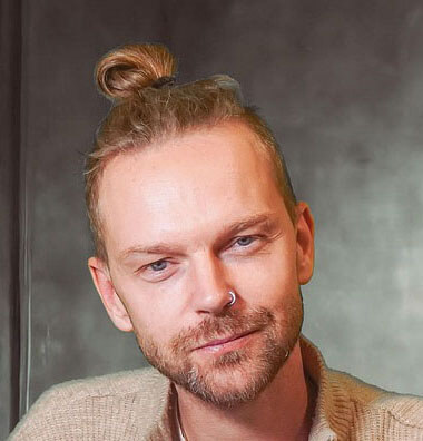 homme aux cheveux clairs attachés en chignon sur le dessus de sa tête. Il porte une barbe et une moustache